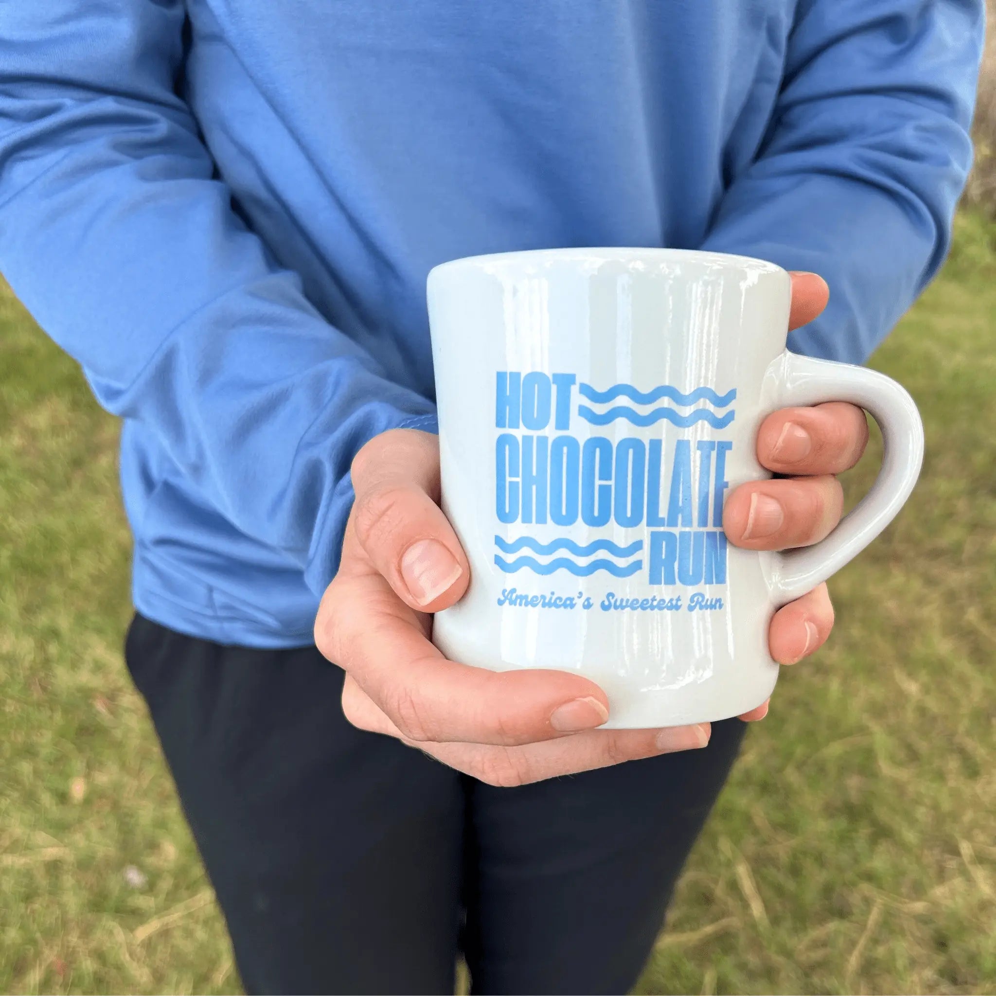 Person holding a white mug with blue Hot Chocolate Run text