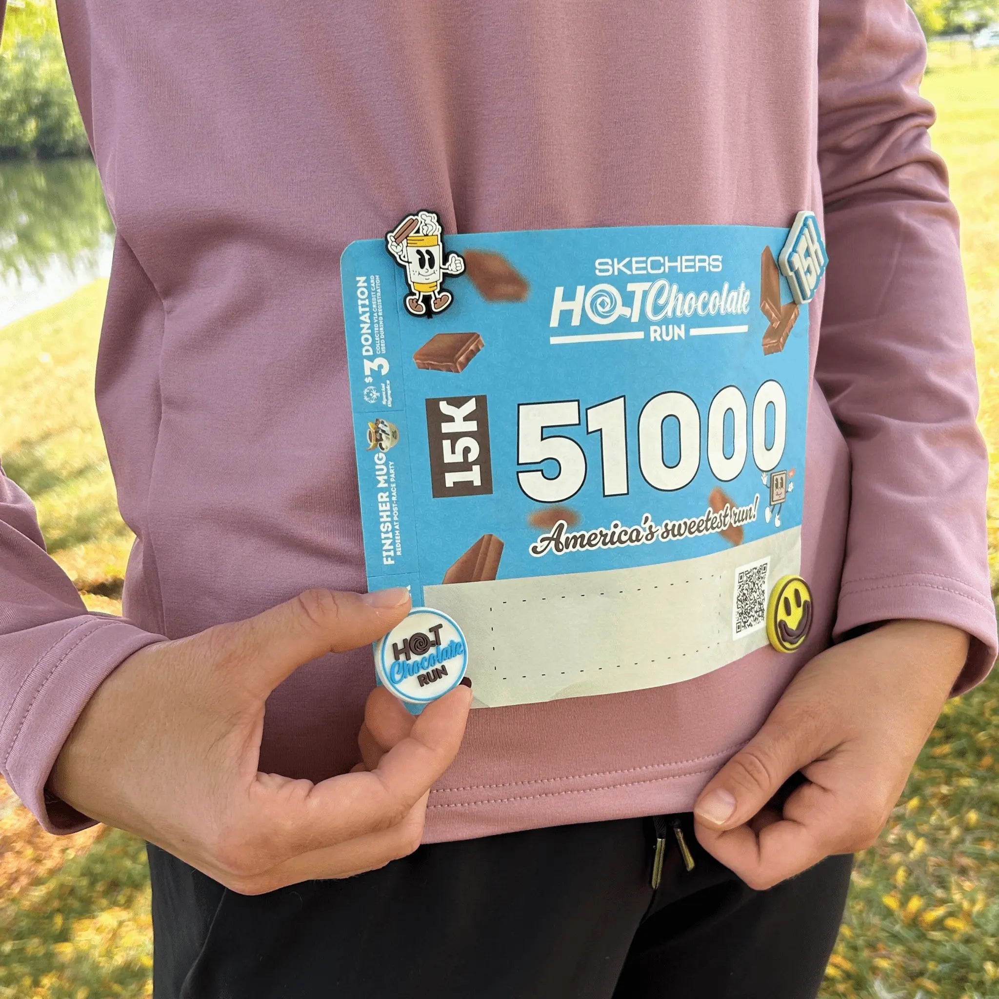 Person outside holding a Skechers Hot Chocolate Run logo mesnap and showing it on the race bib