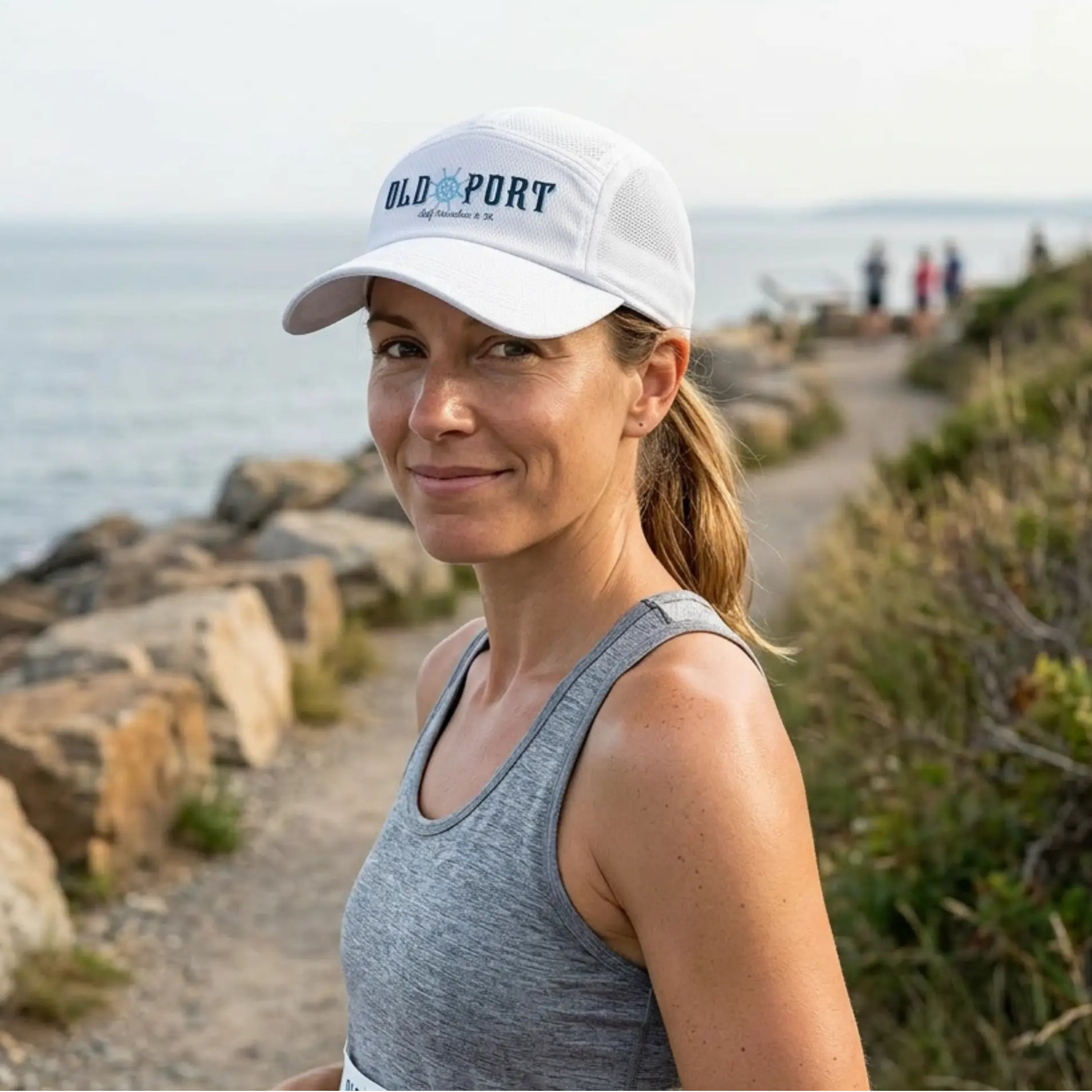 Woman wearing a white cap with 'Old Port' branding by the water