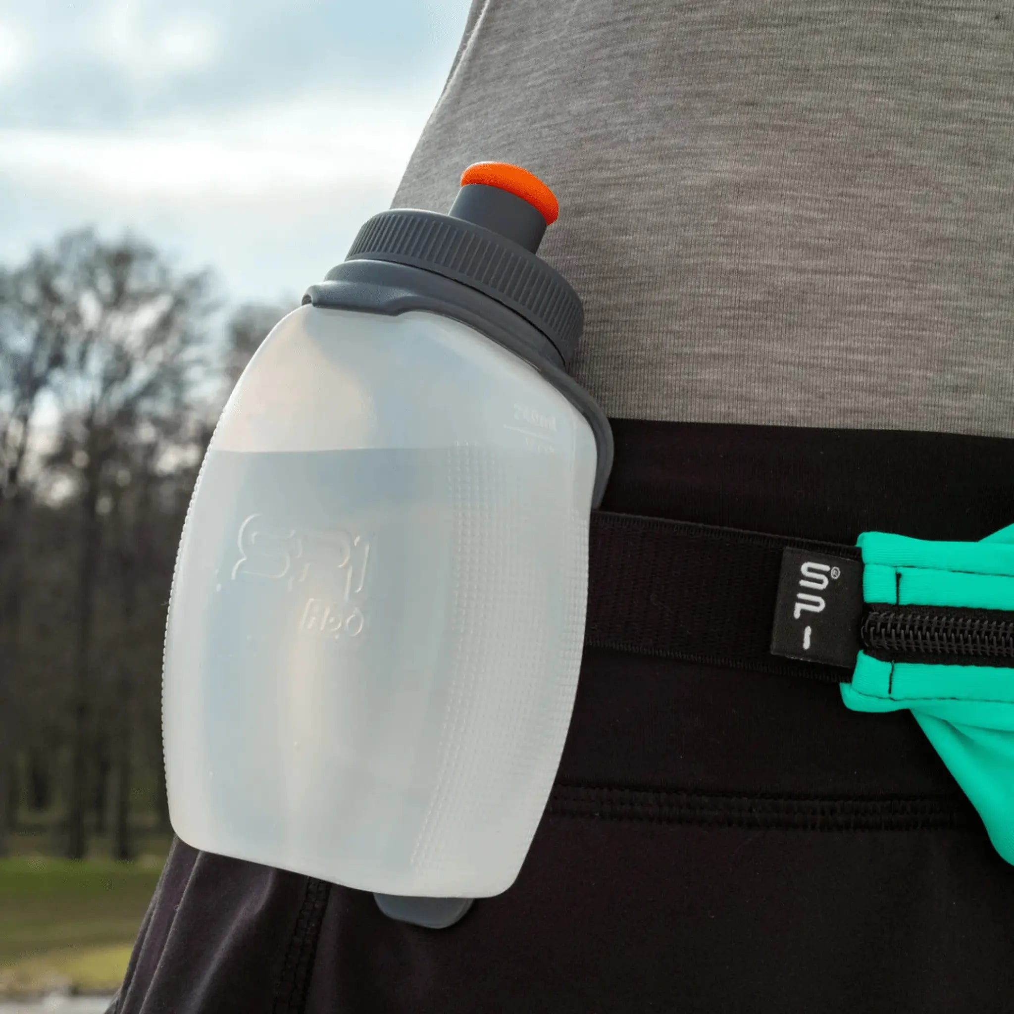 White and black SPI sports bottle with orange cap attached to a person's waist band