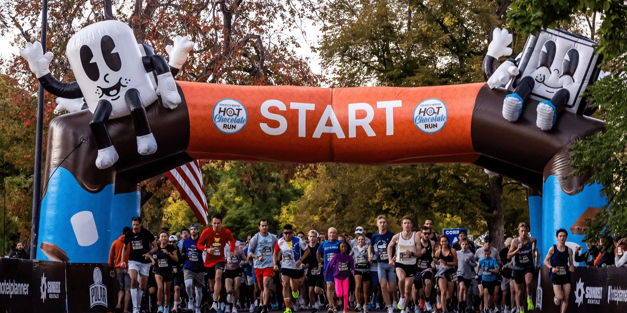 Runners at a starting line with an inflatable START archway featuring Hot Chocolate Run characters