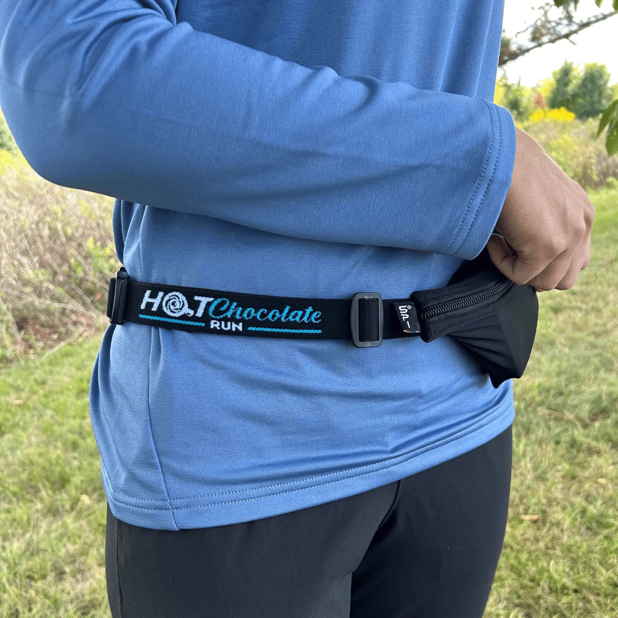 Person wearing a blue jacket with a 'Hot Chocolate Run' belt outdoors
