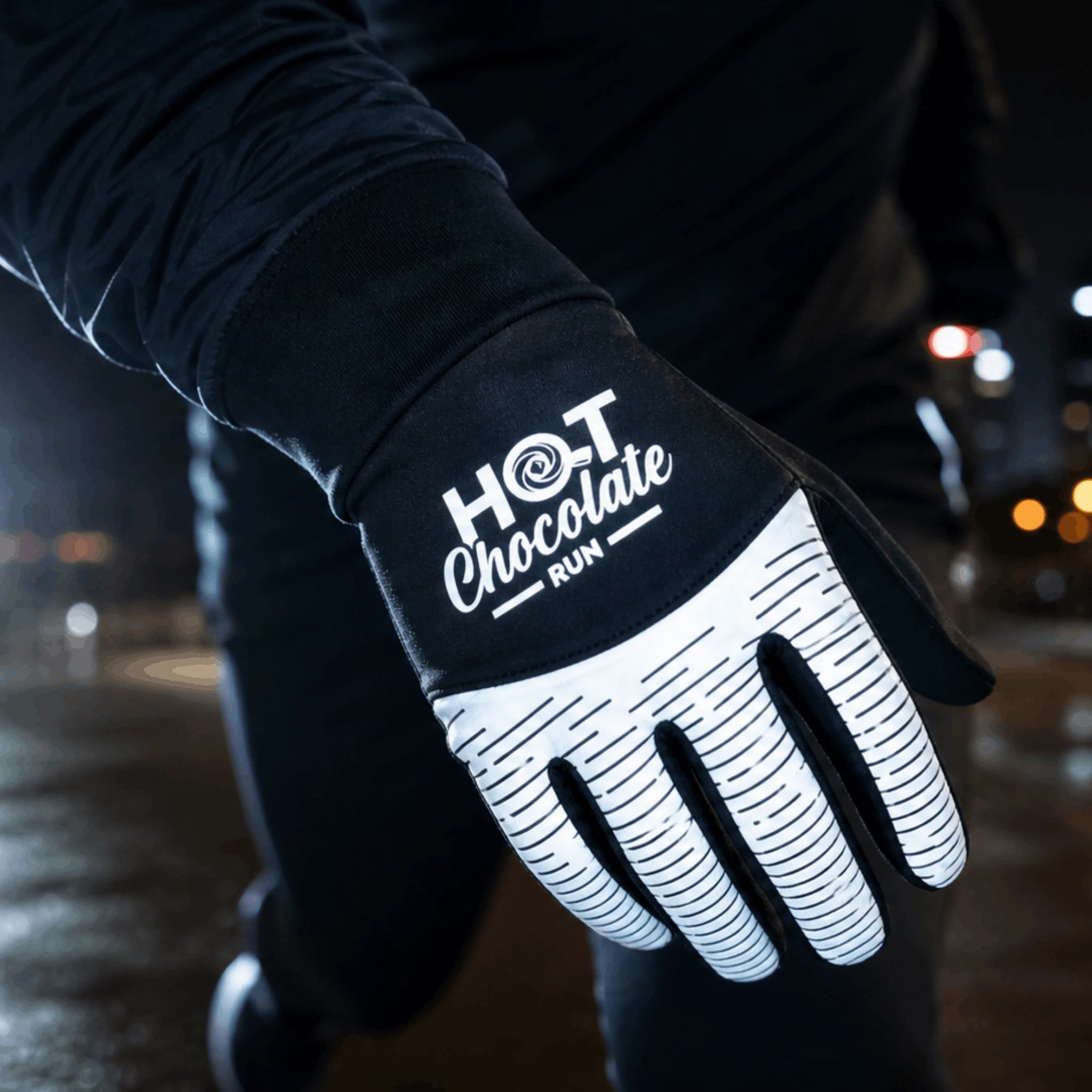 A close-up of a person wearing a black and white reflective running glove with the text 'HOT Chocolate RUN' printed on the back of the hand