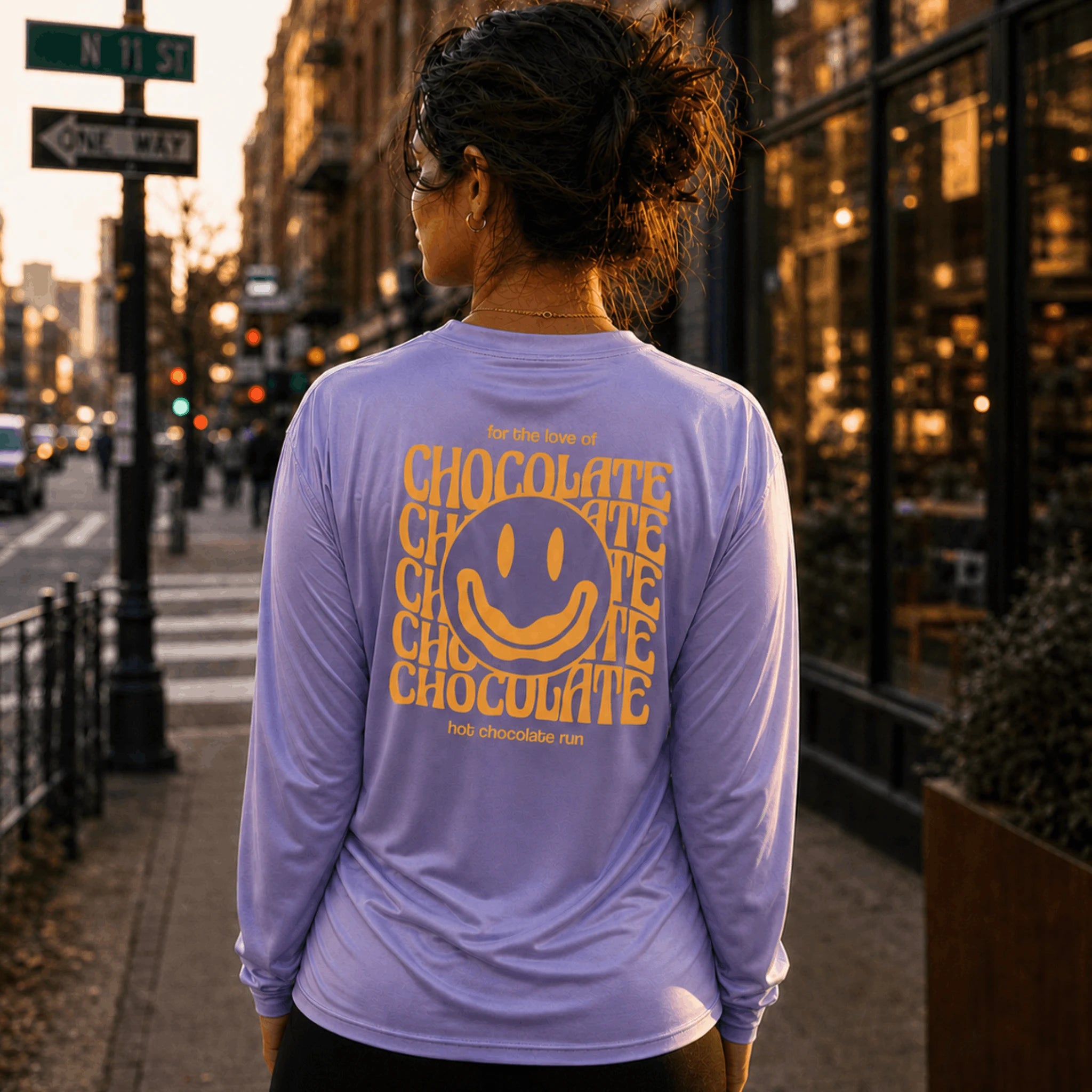 Person wearing a purple shirt with 'Chocolate' text and smiley face design, standing on a city street.