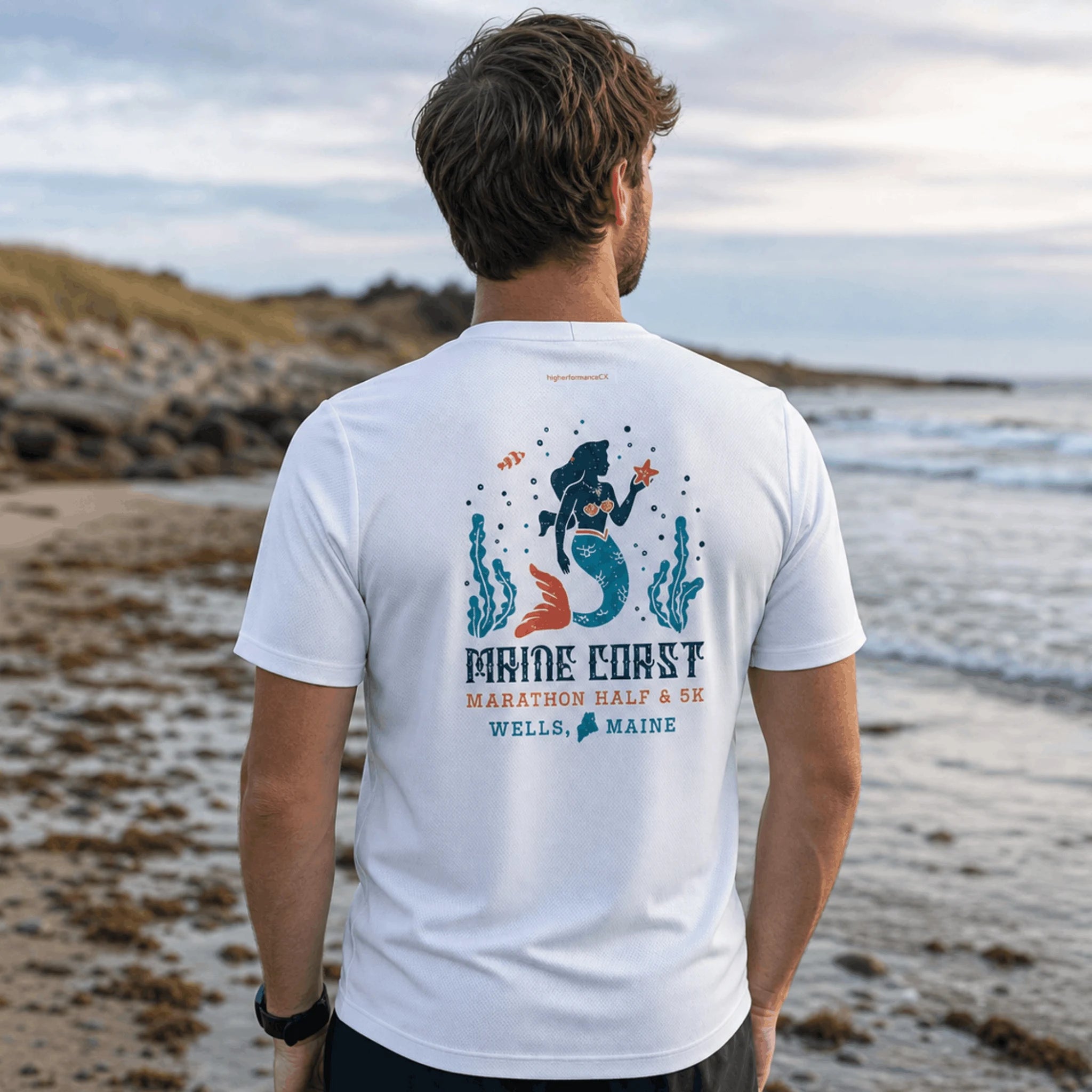 Man wearing white tee with Maine Coast Marathon text and design in beach setting